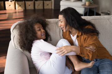 Affectionate caring African American mother tickling laughing adorable preteen curly kid daughter,...