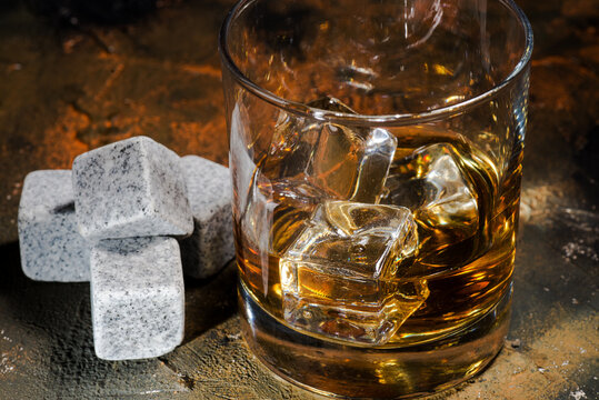 Whiskey with whiskey stones. Glass of whiskey in glass cup with ice cubes on brown background.
