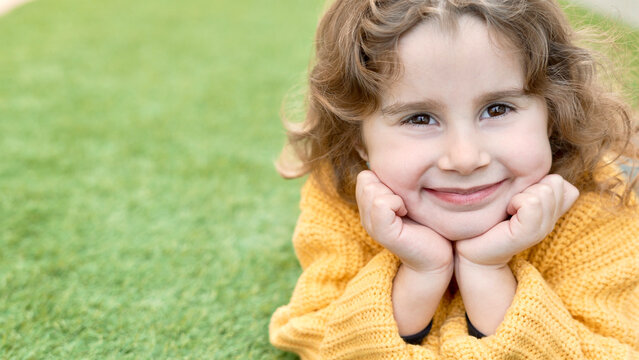 Portrait of a girl smiling and looking at the camera on the artificial synthetic grass in the garden at home enjoying herself. 