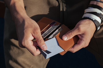 A young man in sportswear is holding a small comfortable red leather wallet in his hands and takes out a plastic card, top view. Horizontal orientation, copy space, close-up, no face - obrazy, fototapety, plakaty