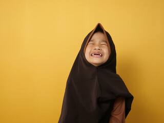 Little cute Asian muslim girl wearing hijab crying hard, sad expression. Against yellow