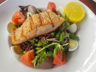 Grilled salmon on top of a salad with lettuce, tomatoes hard boiled eggs, cheese and caesar dressing