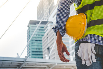 Engineer man hands holding hardhat white work helmet hard hat for Civil Construction Engineering. Construction engineer man in safety suit hold white work helmet hard hat on hands at Construction Site