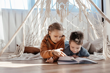 brother and sister are playing at home in a bright sunny room. a teepee toy house. children are...