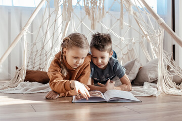 brother and sister are playing at home in a bright sunny room. a teepee toy house. children are...