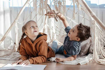 brother and sister are playing at home in a bright sunny room. a teepee toy house. children are...
