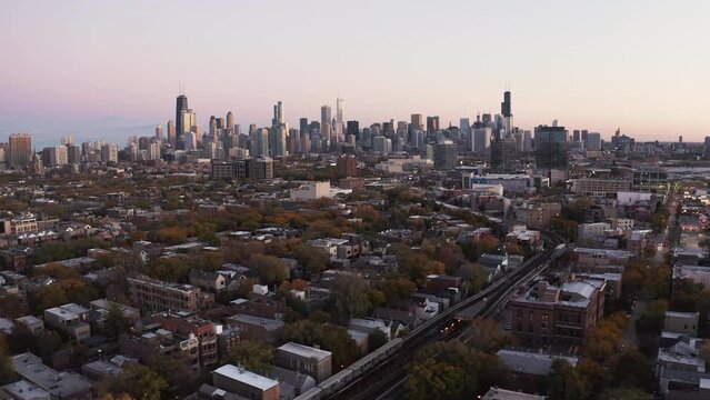 Aerial above Chicago downtown neighborhood with tall skyscrapers on horizon at sunset. Clear sky with city panorama
