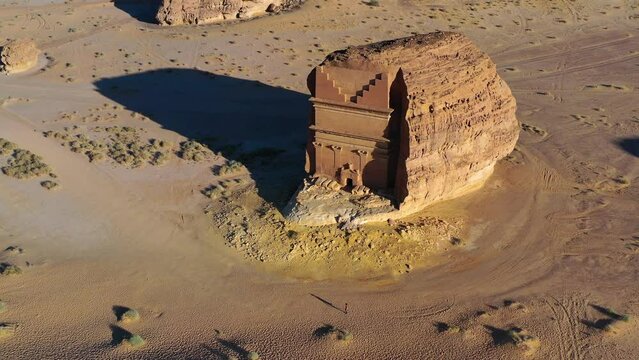 Aerial view of a person walking in front of the Hegra monument, golden hour, in Hejaz, Saudi Arabia - orbit, drone shot