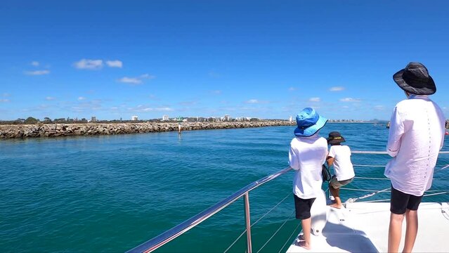 Three lucky young boys standing, looking out at the front of a catamaran yacht. Leaving the Mooloolaba spit in the Sunshine Coast Australia. Slow motion.