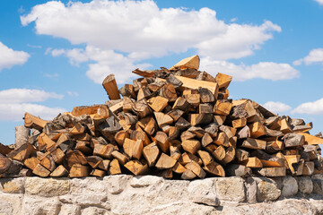 A pile of logs for the stove stacked on top of each other against the blue sky