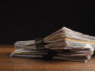 Stack of documents with binder clips on a wooden table with a black background