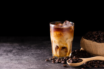 Coffee, iced latte in a glass Add milk or cream along with roasted coffee beans. Set on a wooden table at a coffee shop on a dark black background.