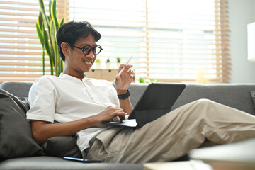 Man relaxing on sofa at home and browsing internet with laptop computer.