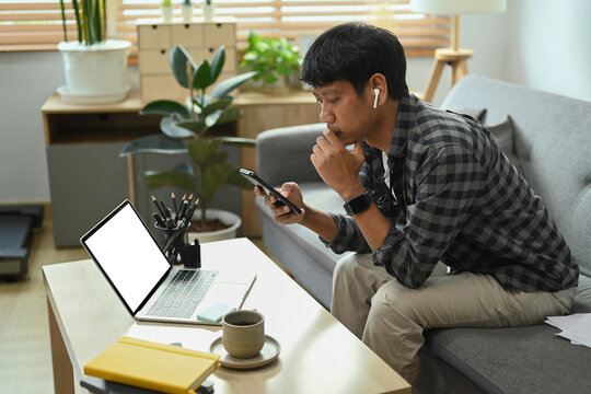 Young man reading message, checking social media on smart phone while spending leisure time at home.