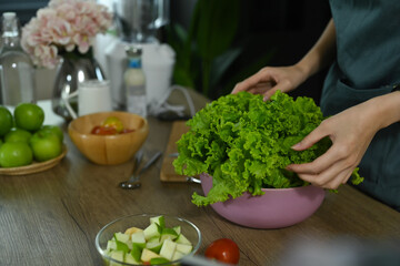 Healthy woman preparing fresh vegetable salad in home kitchen.