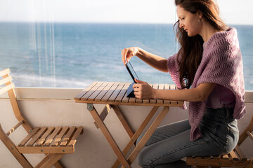 A young woman is working on tablet on the balcony near the sea
