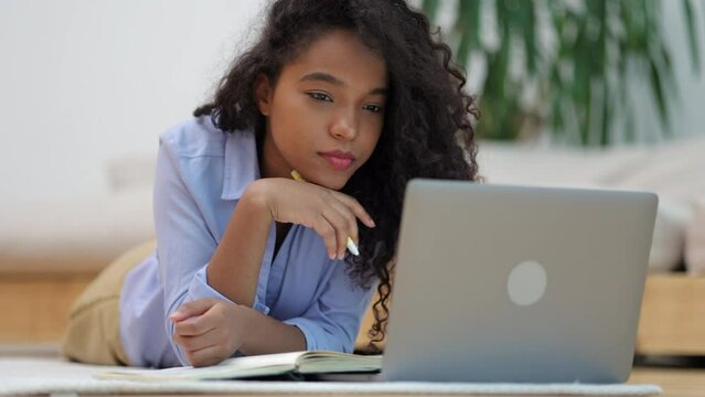 Portrait of female student using laptop and studying online while lying on floor at home spbi. 4k video Close view of young african american woman looks at computer screen with smile and surfs web