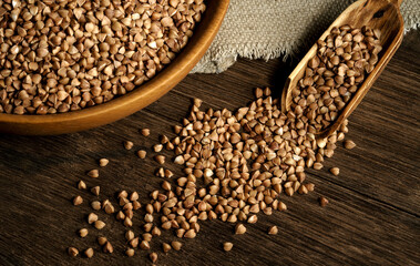 Organic buckwheat groats in a wooden bowl with a spoon on a linen napkin on a wooden table. Banner. Rustic style. Healthy nutrition concept. Buckwheat contains a large amount of vitamins and minerals.