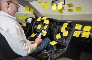 Fototapeta premium A man working in the driver's seat of a car surrounded by many to-do notes.