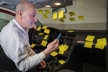 A man working in the driver's seat of a car surrounded by many to-do notes.