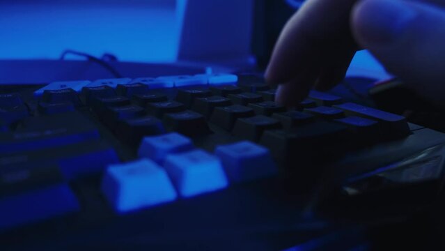 Close-up of a gamer using a keyboard to play games and work against a bright blue background. High quality 4k footage