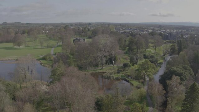 The skyline of Birr, Co. Offaly, surrounded by the vast green countryside on every side featuring trees, hills and a lake. This drone shot slowly rises to reveal the area beyond the immediate trees.