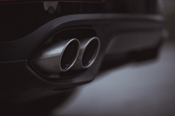 Double oval exhaust tips on a modern sport car or SUV. Visible two tailpipes coming out from an...