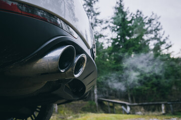 Double oval exhaust tips on a modern SUV car or crossover vehicle. Visible vapour of smoke in green environment. SUV and cars polluting environment. - obrazy, fototapety, plakaty