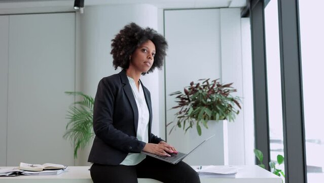 Young businesswoman working with laptop and sitting at table in modern office spbi. 4k video Portrait of american african woman looks at computer screen and types on keyboard, does work and sits on