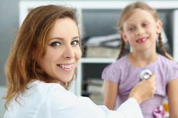 Fototapeta premium Smiling pediatrician doctor listen to girl breath and heartbeat with stethoscope