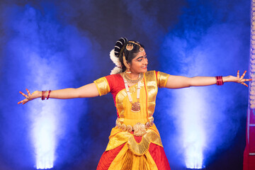 Smiling indian bharatanatyam dancer on stage performing dance with hands gesture - conept of...
