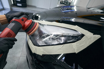 Gloved hands polishing headlight with orbital buffer