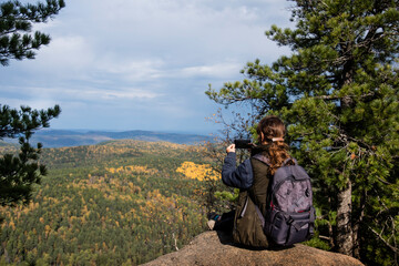 A girl sits on a mountain ledge, admiring the autumn foliage on the neighboring mountains. Beautiful landscape, tourism