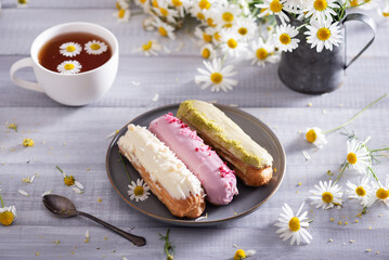 Beautiful delicious french eclairs set with original cream decor on white plate on  wooden background. Selective focus. Tasty colorful dessert profiteroles.