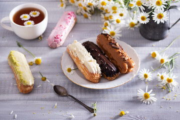 Beautiful delicious french eclairs set with original cream decor on white plate on  wooden background. Selective focus. Tasty colorful dessert profiteroles.