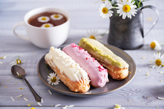 Beautiful delicious french eclairs set with original cream decor on white plate on  wooden background. Selective focus. Tasty colorful dessert profiteroles.