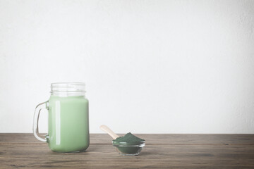 fresh green smoothie in glass bottle and spirulina powder with spoon on wooden background. useful habits, self care and healthy lifestyle. copy space