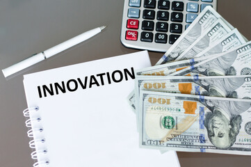 INNOVATION text on a notebook on an office desk, next to it is a calculator, a backpack and dollar bills