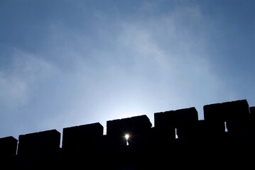A sunstar peeks through a hole in the ramparts of the Old City of Jerusalem in silhouette at...
