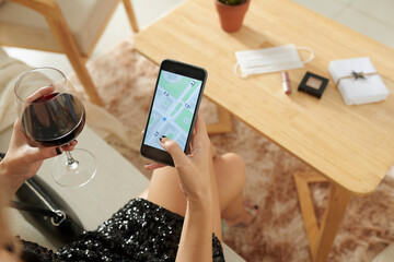 Woman finishing glass of wine and ordering taxi car via application on smartphone