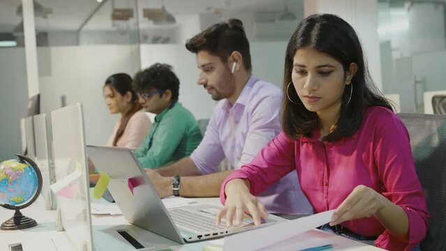 Indian diverse businesswoman people with documents and gadgets sitting in row. Office workers sitting in table and working on tablet or reading report .