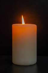 White burning pillar candle standing on gold decorated saucer on dark dining table