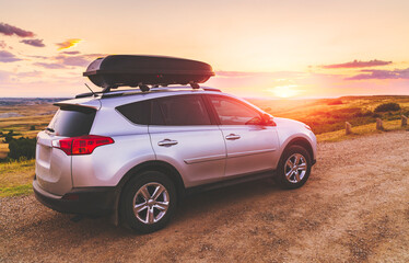 Fototapeta na wymiar SUV with roof box dive on dirt road at sunset.