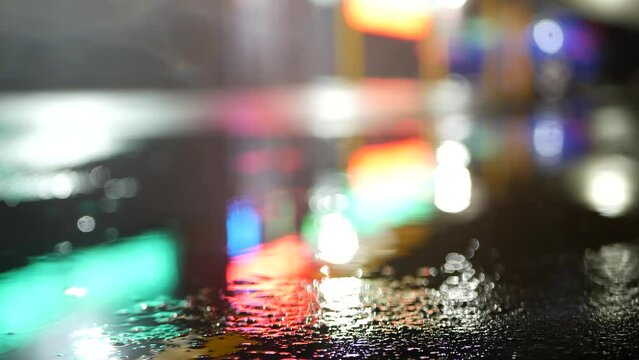 Neon lights reflection on road in rainy weather. Rain drops on wet asphalt of city street in USA. Puddle of water on pavement or sidewalk. Rainfall at night. Abstract seamless looped cinemagraph.