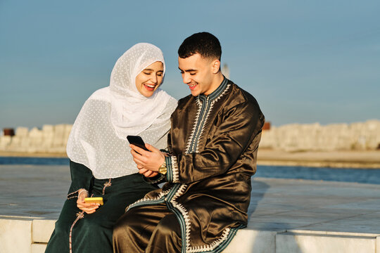 Happy woman sitting by man using smart phone on sunny day