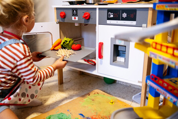 Son putting vegetables tray by oven in toy kitchen at home