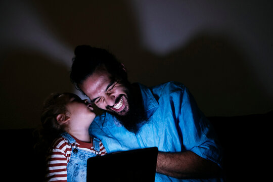 Son whispering in happy father's ear in front of tablet PC at home