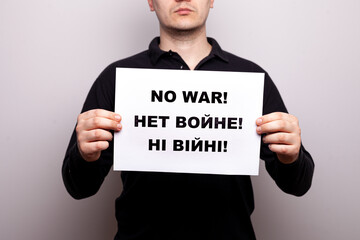 No war in three languages - English, Russian, Ukrainian. Aman in a black T-shirt holds a poster with appeals for peace on a white background. no face, close-up. a message not to use aggression.