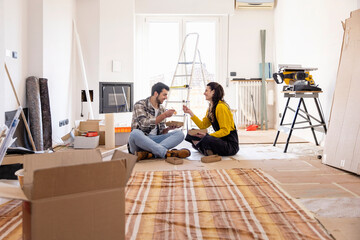 Young couple eating food sitting on ground at new home
