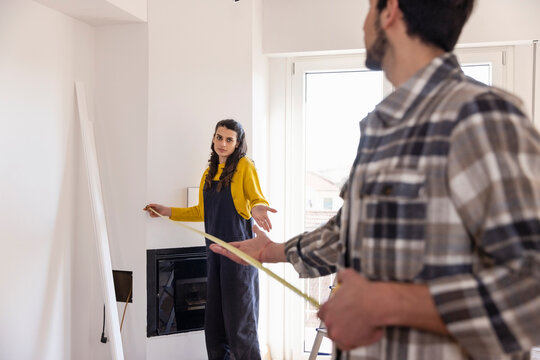 Confused woman with measuring tape talking with boyfriend in new living room